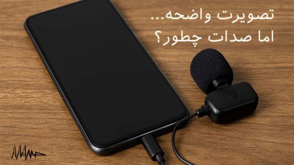 آکادمی صدابازار 6 نمایی دیجیتال از یک گوشی هوشمند مدرن با فریم فلزی و طراحی مات، قرار گرفته بر روی سطح چوبی گرم با میکروفونی جداگانه متصل به درگاه شارژ گوشی، در محیطی با نور ملایم و پسزمینه محو